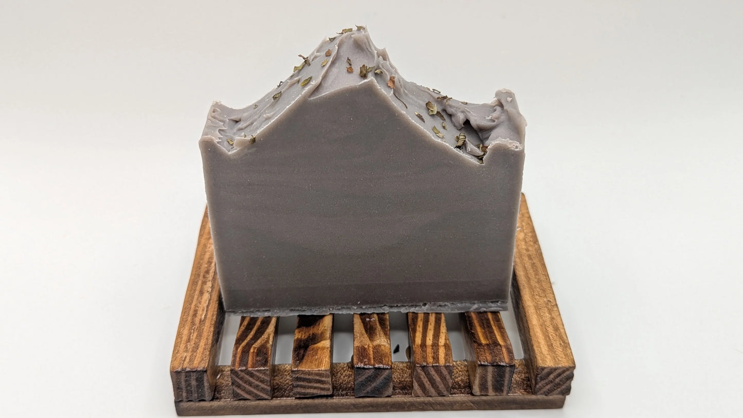 Handcrafted lavender soap bar with textured top and herbs on wooden soap dish