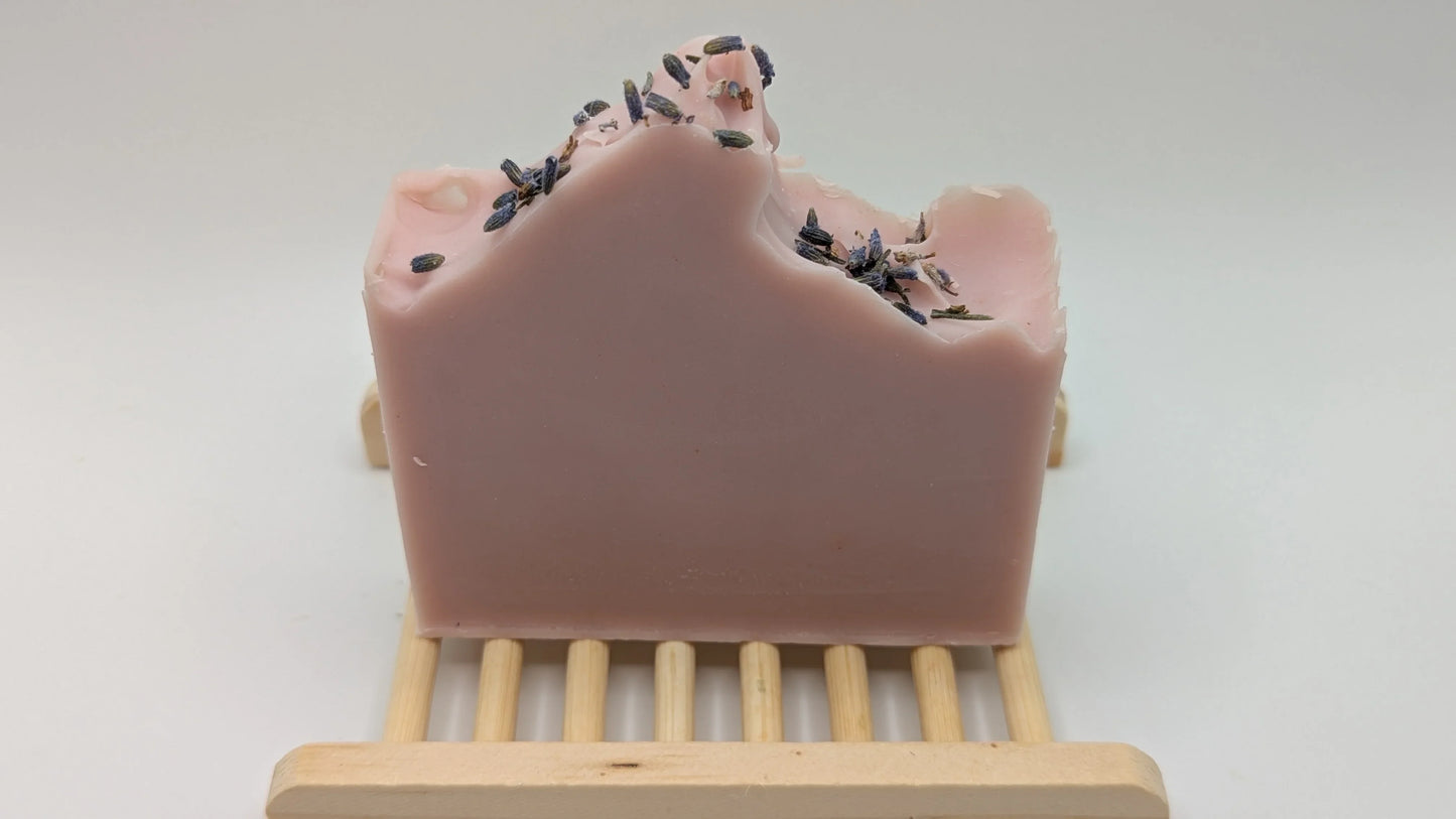 Handcrafted pink lavender soap bar with dried lavender buds on a wooden soap dish
