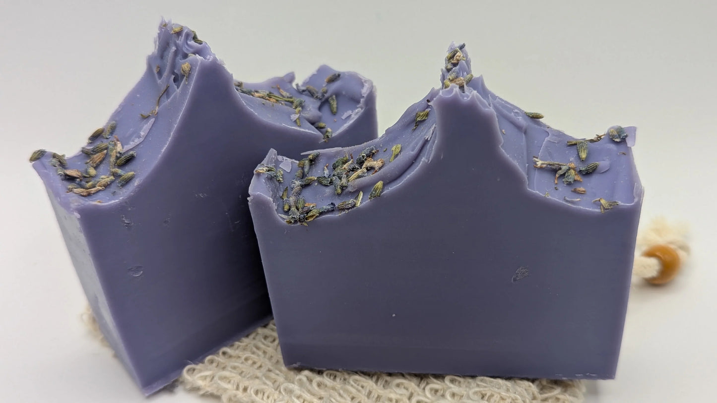 Handcrafted lavender soap bars with dried lavender buds on top, displayed on a textured mat