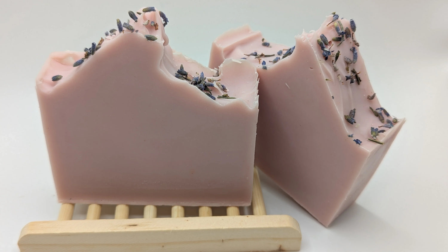Handcrafted pink essential oil soap bars with dried lavender on a wooden soap dish